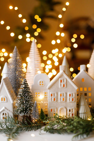 Merry Christmas! Stylish Christmas miniature holiday village with houses, trees, fir branches on background of golden lights bokeh in evening. Atmospheric magical scene. Holiday bannerの写真素材