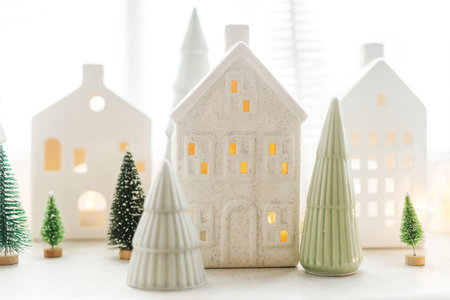 Christmas glowing little ceramic houses and white snowy trees on window. Xmas background. Merry Christmas! Atmospheric Christmas scene, miniature holiday village. Holiday modern decorationsの写真素材