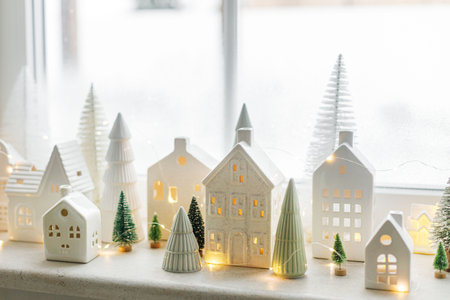 Christmas still life, miniature winter holiday village. Merry Christmas and Happy Holidays! Christmas glowing white little ceramic houses and snowy trees on window. Festive stylish decorationの写真素材
