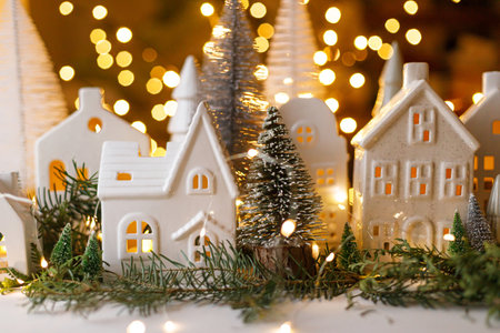 Christmas little ceramic houses, trees and lights on dark background with golden bokeh in eve. Merry Christmas! Atmospheric Christmas scene, miniature holiday village. Xmas backgroundの写真素材