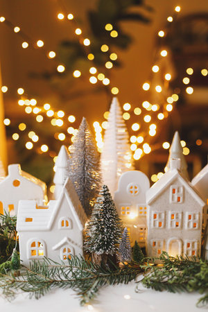 Christmas little ceramic houses, trees and lights on dark background with golden bokeh in eve. Merry Christmas! Atmospheric Christmas scene, miniature holiday village. Xmas backgroundの写真素材