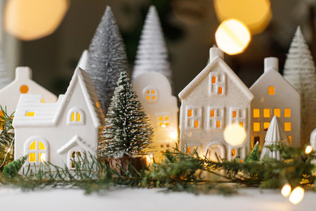 Merry Christmas! Stylish Christmas miniature holiday village with houses, trees, fir branches and golden lights bokeh in evening room. Atmospheric magical scene. Christmas holiday bannerの写真素材