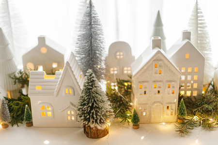 Christmas little ceramic houses, white snowy trees and golden lights on window in eve. Merry Christmas! Atmospheric Christmas scene, miniature holiday village. Xmas backgroundの写真素材