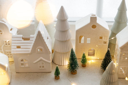 Christmas little ceramic houses, white snowy trees and golden lights on window. Xmas background. Merry Christmas! Atmospheric Christmas scene, miniature holiday villageの写真素材