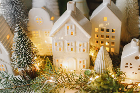 Merry Christmas! Stylish Christmas miniature holiday village with houses, trees, fir branches and golden lights bokeh in evening room. Atmospheric magical scene. Christmas holiday bannerの写真素材