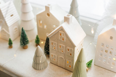 Merry Christmas! Stylish Christmas miniature holiday village with white houses, trees and golden lights bokeh on snowy window. Atmospheric magical scene. Christmas holiday banner.の写真素材