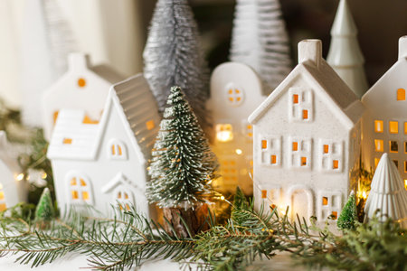 Christmas still life, miniature winter holiday village. Merry Christmas and Happy Holidays! Christmas white little houses, trees and lights on table with fir branches. Atmospheric magical eveの写真素材