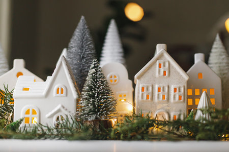 Merry Christmas! Stylish Christmas miniature holiday village with houses, trees, fir branches and golden lights bokeh in evening room. Atmospheric magical scene. Christmas holiday bannerの写真素材