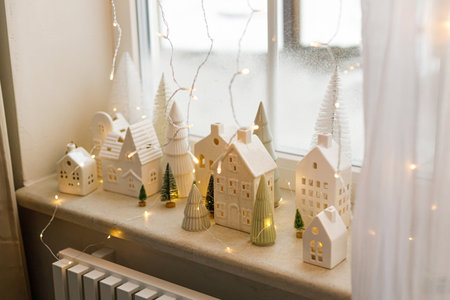 Christmas little ceramic houses, white snowy trees and golden lights on window. Xmas background. Merry Christmas! Atmospheric Christmas scene, miniature holiday villageの写真素材