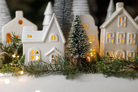Christmas still life, miniature winter holiday village. Merry Christmas and Happy Holidays! Christmas white little houses, trees and lights on table with fir branches. Atmospheric magical eveの写真素材