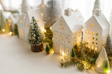 Christmas little ceramic houses, white snowy trees and golden lights on window in eve. Merry Christmas! Atmospheric Christmas scene, miniature holiday village. Xmas backgroundの写真素材