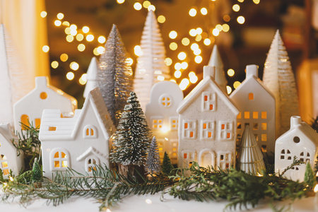 Merry Christmas! Stylish Christmas miniature holiday village with houses, trees, fir branches on background of golden lights bokeh in evening. Atmospheric magical scene. Holiday bannerの写真素材