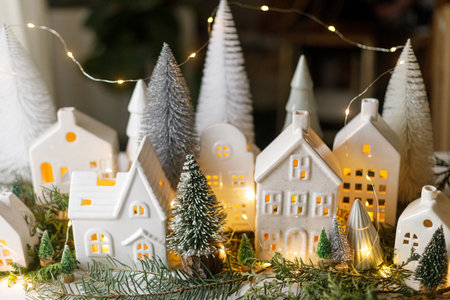 Christmas little ceramic houses, snowy trees and golden lights on dark background in eve. Merry Christmas! Atmospheric Christmas scene, miniature holiday village. Xmas backgroundの写真素材