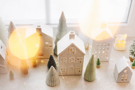 Christmas little ceramic houses, white snowy trees and golden lights on window. Xmas background. Merry Christmas! Atmospheric Christmas scene, miniature holiday villageの写真素材
