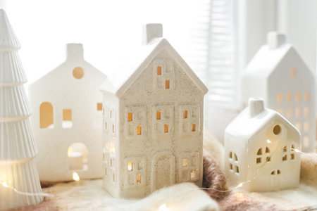 Merry Christmas! Stylish Christmas miniature holiday village with glowing golden lights on cozy blanket at snowy window. Atmospheric magical scene. Christmas holiday banner.の写真素材