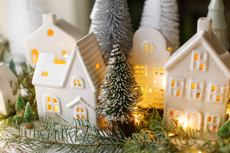 Christmas still life, miniature winter holiday village. Merry Christmas and Happy Holidays! Christmas white little houses, trees and lights on table with fir branches. Atmospheric magical eveの写真素材
