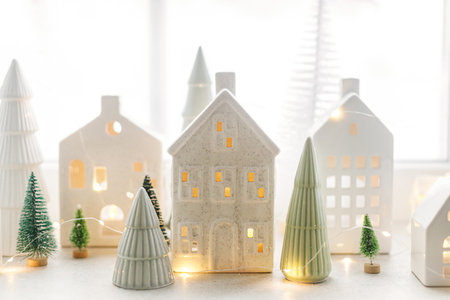 Christmas little ceramic houses, white snowy trees and golden lights on window. Xmas background. Merry Christmas! Atmospheric Christmas scene, miniature holiday villageの写真素材
