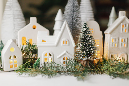 Merry Christmas! Stylish Christmas miniature holiday village with houses, trees, fir branches and golden lights bokeh in evening room. Atmospheric magical scene. Christmas holiday bannerの写真素材