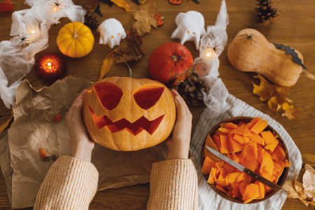 Happy Halloween! Carving halloween pumpkin. Woman holding pumpkin and knife on table with ghosts and spiders. Making halloween decorationsの写真素材