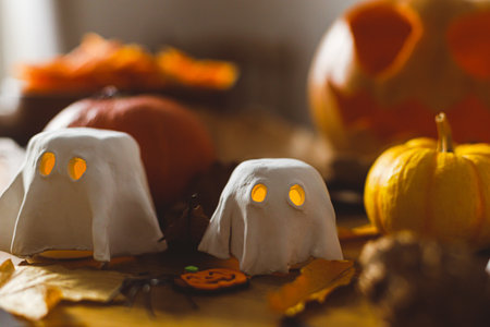 Happy Halloween! Cute glowing ghosts, Jack o lantern pumpkin and spiders on table in living room. Spooky atmospheric halloween decorations, space for text.の写真素材