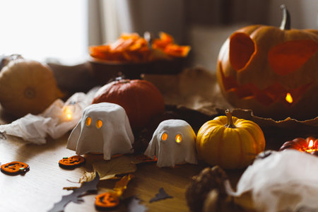 Happy Halloween! Cute glowing ghosts, Jack o lantern pumpkin and spiders on table in living room. Spooky atmospheric halloween decorations, space for text.の写真素材