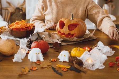 Happy Halloween! Carving halloween pumpkin. Woman holding pumpkin and knife on table with ghosts and spiders. Making halloween decorationsの写真素材