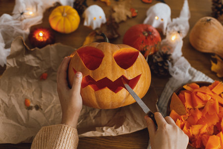 Making jack o lantern. Woman carving halloween pumpkin on table with ghosts and spiders, halloween preparation. Happy halloween! Making festive decorationsの写真素材