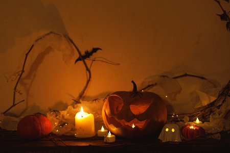 Happy Halloween! Spooky Jack o lantern pumpkin, glowing ghosts, spiders and bats in dark. Atmospheric halloween decor on table. Trick or treatの写真素材