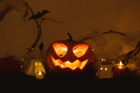 Happy Halloween! Spooky Jack o lantern pumpkin, glowing ghosts, spiders and bats in dark. Atmospheric halloween decor on table. Trick or treatの写真素材