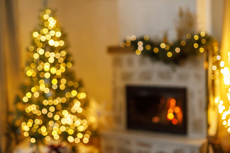 Xmas background. Blurred image of stylish christmas tree with golden lights bokeh and burning fireplace in evening living room. Defocused atmospheric christmas eve at home.の写真素材
