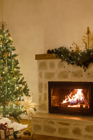 Stylish decorated christmas tree with vintage ornaments and modern decor of fireplace mantel with bells, ribbon and garland lights in evening. Atmospheric christmas eve at home. Merry Christmas!の写真素材