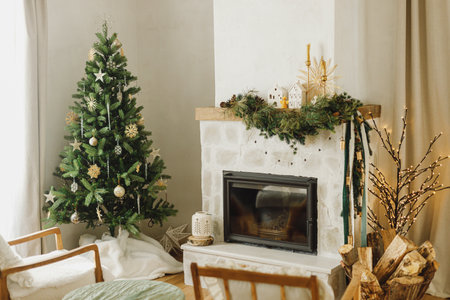 Stylish decorated christmas tree with vintage ornaments and modern decor of fireplace mantel with fir branch, bells, ribbon and garland light. Atmospheric xmas holidays at home. Merry Christmas!の写真素材
