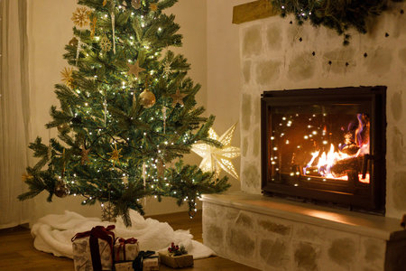 Stylish decorated christmas tree with vintage ornaments and modern decor of fireplace mantel with bells, ribbon and garland lights in evening. Atmospheric christmas eve at home. Merry Christmas!の写真素材