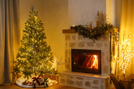 Merry Christmas! Stylish decorated christmas tree with vintage ornaments and modern decor of fireplace mantel with bells, ribbon and garland lights in evening. Atmospheric christmas eve at homeの写真素材