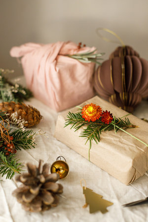 Zero waste Christmas. Stylish christmas gifts wrapped in fabric and paper with fir branches on rustic table with natural ornaments. Winter eco holiday, modern presents. Merry Christmasの写真素材