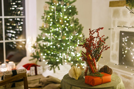 Merry Christmas! Stylish christmas gift, ornaments and candles on table on background of xmas tree with lights and stylish gifts under xmas tree in evening room. Atmospheric christmas eve at homeの写真素材