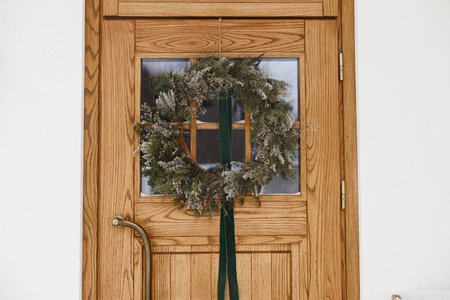Stylish christmas rustic wreath with ribbon hanging on wooden doors, close up. Modern farmhouse entrance decoration for winter holiday. Merry Christmas and Happy holidaysの写真素材