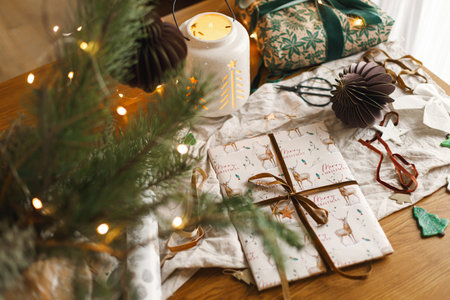 Stylish christmas glowing lantern, gift and modern paper ornaments on rustic table with golden...