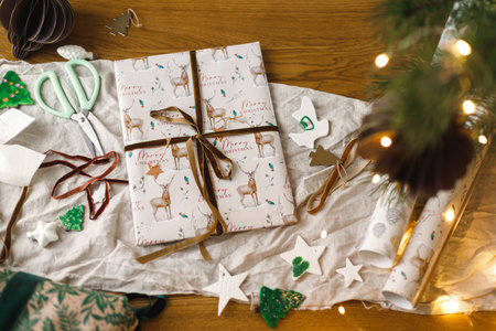 Stylish christmas gifts flat lay, modern paper ornaments and pine branches on rustic table with golden lights bokeh. Merry Christmas! Atmospheric christmas preparation, wrapping presentsの写真素材