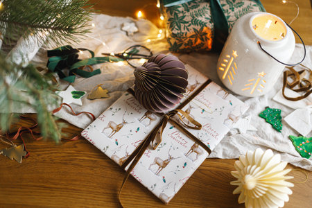 Merry Christmas and Happy holidays! Stylish christmas gift, glowing lantern, modern paper ornaments on table with golden lights, top view. Atmospheric christmas eve, holiday magical timeの写真素材