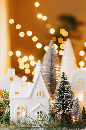 Merry Christmas! Stylish Christmas miniature holiday village with houses, trees, fir branches on background of golden lights bokeh in evening. Atmospheric magical scene. Holiday bannerの写真素材