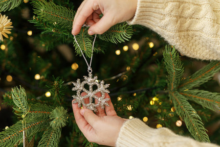 Decorating christmas tree with vintage ornaments. Hands in cozy sweater hanging stylish Christmas star on christmas tree with golden lights. Merry Christmasの写真素材