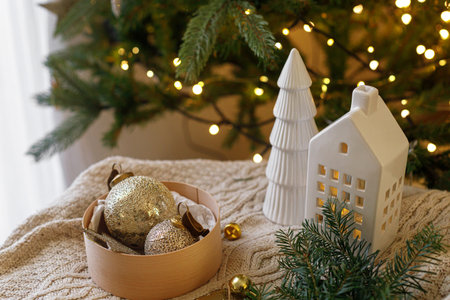 Decorating christmas tree with vintage golden baubles. Stylish Christmas ornaments in box on knitted blanket with fir branches on background of christmas tree with lights. Merry Christmasの写真素材