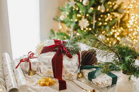 Stylish christmas gift box with red ribbon, spruce branch and modern ornaments on background of decorated christmas tree. Merry Christmas and Happy Holidays. Modern Christmas presentの写真素材