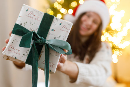 Stylish christmas gift box in hands of happy woman at christmas tree with golden lights. Merry Christmas and Happy Holidays! Exchanging presents surpriseの写真素材