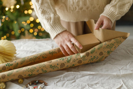 Wrapping stylish christmas gift, winter holidays preparation. Woman in cozy sweater holding gift box...