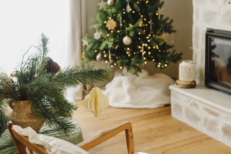 Stylish christmas decorated living room with christmas tree, modern fireplace, fir branch with ornaments and garland light. Atmospheric xmas holidays at home. Merry Christmas!の写真素材
