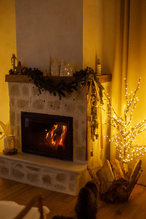 Stylish christmas tree with golden lights in modern living room with festive decorated fireplace mantel. Festive xmas scandinavian room. Atmospheric magical eveの写真素材
