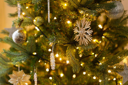 Stylish christmas ornaments on tree close up. Beautiful decorated christmas tree with straw snowflake, vintage baubles and golden lights. Winter holidays preparation. Atmospheric magical eveの写真素材