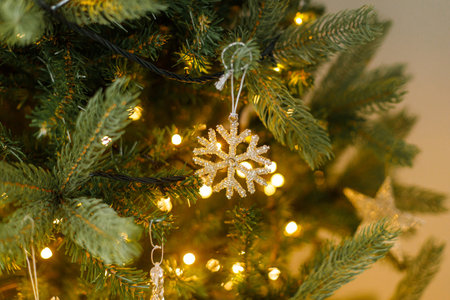 Stylish christmas ornament on tree close up. Beautiful decorated christmas tree with glass snowflake, vintage baubles and golden lights. Winter holidays preparation. Atmospheric magical eveの写真素材